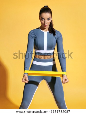 Sporty woman performs exercises for the muscles of the hands. Photo of woman workout with resistance band on yellow background. Strength and motivation.