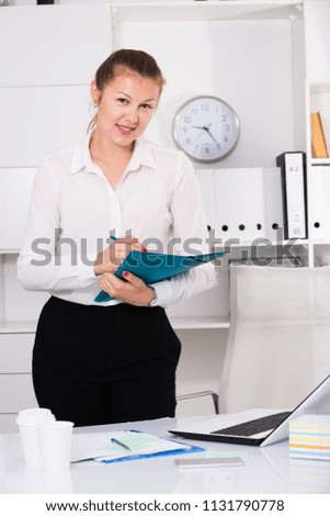 Office manager woman is signing agreement papers of financial nature at office.