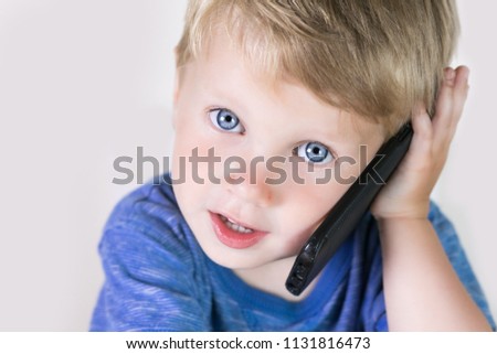 Little kid boy with mobile phone in hands, looking in it and talking on white background. Children and smartphone, new technology concept