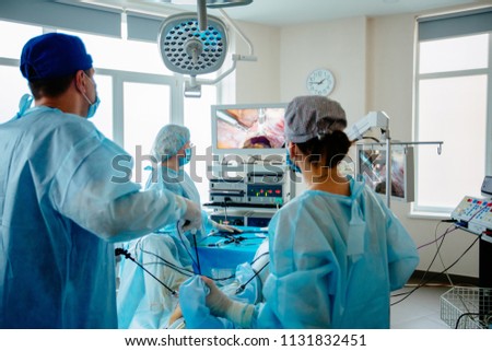 Back view of surgeons team looks at monitors while preforming operation in hospital operating theater, male surgeon operating patient working with surgical laparoscopy instruments. Gynecology. Royalty-Free Stock Photo #1131832451