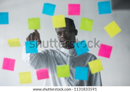 Young afro american business man standing in front of stickers glass wall and pointed choose on right sticker at his office place