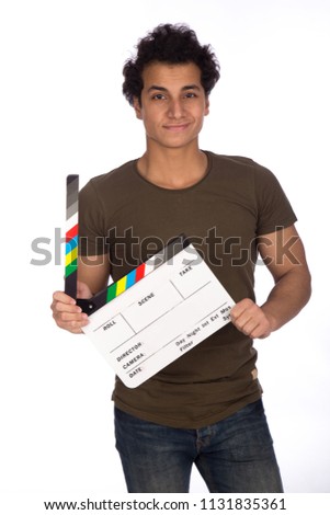 Handsome young man wearing a casual outfit, standing and holding a clapperboard, on his face big smile, isolated on white background.