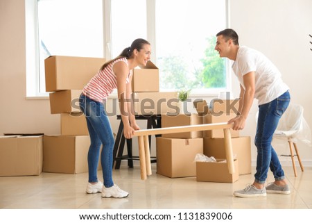 Young couple carrying table in room after moving to new home Royalty-Free Stock Photo #1131839006