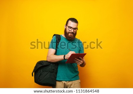 Young bearded hipster man using tablet standing over yellow background