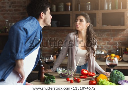 Happy couple cooking and tasting healthy food in their loft kitchen at home. Woman and man drinking wine. Preparing vegetable salad.