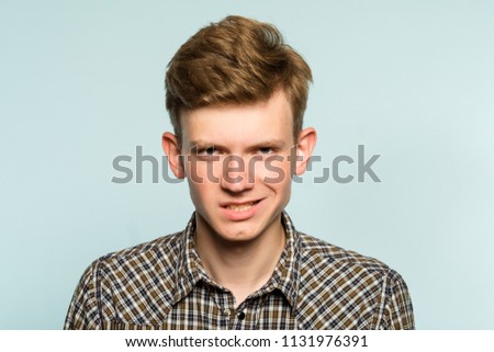 threatening intimidating sneer. crazy looking man with a smirk. portrait of a young guy on light background. emotion facial expression. feelings and people reaction. Royalty-Free Stock Photo #1131976391