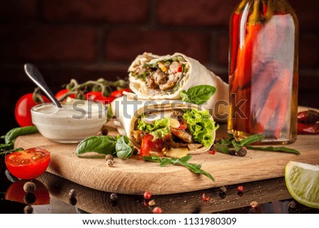 Mexican cuisine, burrito with chicken, cherry tomatoes, lettuce, mushrooms, rucola and chili peppers, on a black background. With salsa sauce. Copy space, selective focus