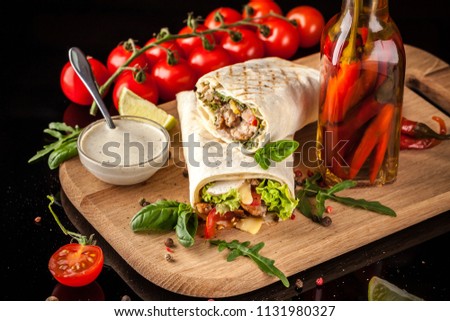 Mexican cuisine, burrito with chicken, cherry tomatoes, lettuce, mushrooms, rucola and chili peppers, on a black background. With salsa sauce. Copy space, selective focus