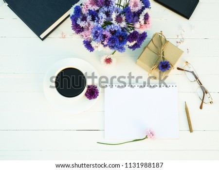Coffee Time. Sketchbook for greeting message with a Cup of Coffee, Gift Box,  Summer Cornflowers Flowers, glasses, book and smartphone on white table