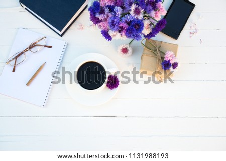 
Coffee Time. Cup of Coffee, Gift Box, Summer Cornflowers Flowers, Sketchbook, glasses, book and smartphone on white table