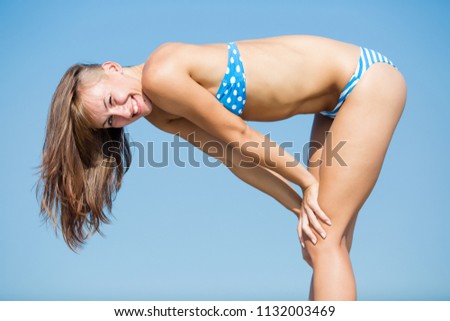 Athletic girl in blue bikini posing bent leaning on her knees. She winking looking at camera smiling 