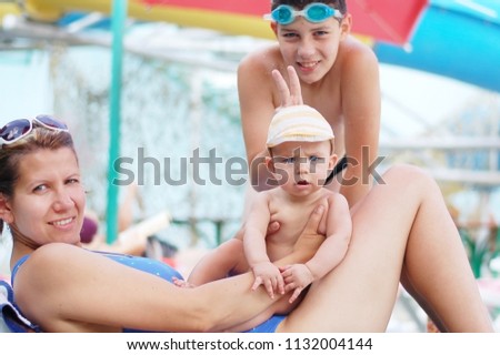 A beautiful mother with two sons resting at the pool on a sunny day. They are happy with the wonderful weather and the fact that together spend fun time