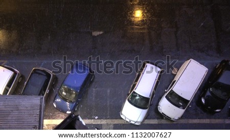 Top down picture of city streets at night and heavy rainfall and thunderstorm flashes illuminating the streets and parked cars for short period of time typical city scene during rain season
