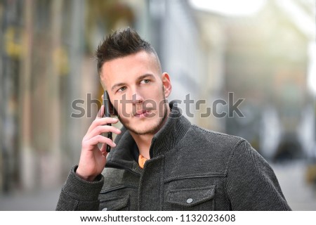 young man talking on mobile phone on street in autumn