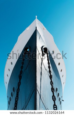 a view of the bow of a moored ship, painted white and navy, against the blue sky Royalty-Free Stock Photo #1132026164