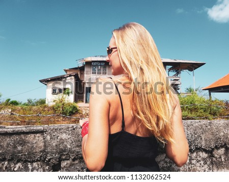 Back view of woman looking at the abandoned building behind barbwire fence in sunny summer day