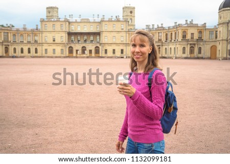 Smiling woman with coffee in a paper cup on the background of architectural attractions.