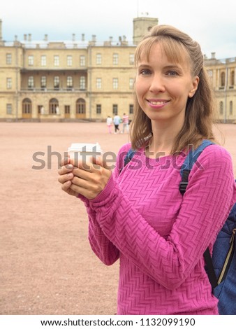 Smiling woman with coffee in a paper cup on the background of architectural attractions.