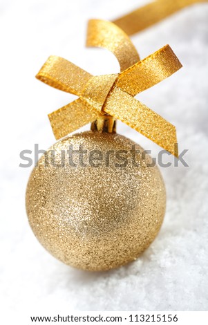 Closeup of a shiny gold glitter Christmas bauble with a decorative golden ribbon and bow on snow