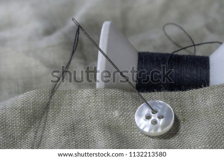 Close up of needle with black thread and white sewing button.