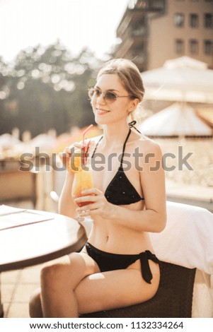 Blonde woman in bikini sitting on a terrace with a drink on a vacation.