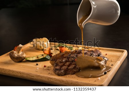 Gravy pouring over grilled seasoned meat, isolated on black Royalty-Free Stock Photo #1132359437