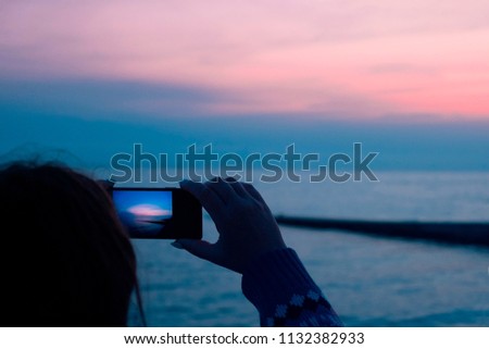 girl takes a picture on mobile phone sunset in the evening at sea