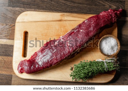 Raw fresh beef meat fillet on wooden cutting desk with herbs and salt. Top flat lay view, from above.