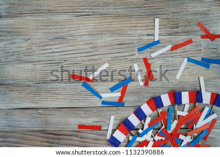 Paper confetti of the national colors of France, white-blue-red on a white wooden background with flags, concept Bastille day