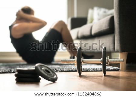 Home workout. Man doing ab training and crunches in living room gym. Guy doing sit ups. Warm up before weight exercise. Fitness concept with dumbbell and athlete. Royalty-Free Stock Photo #1132404866