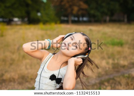 beautiful girl with long hair dancing outdoor, pretty child with black and silver headphone listening music on meadow