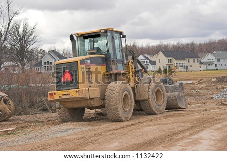 Color DSLR picture of yellow heavy industrial construction equipment, a bulldozer, at a new home residential construction site. Horizontal orientation with copy space for text.