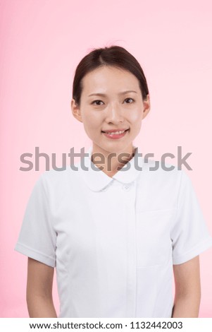 Woman wearing white uniform smiling in front of pink background
