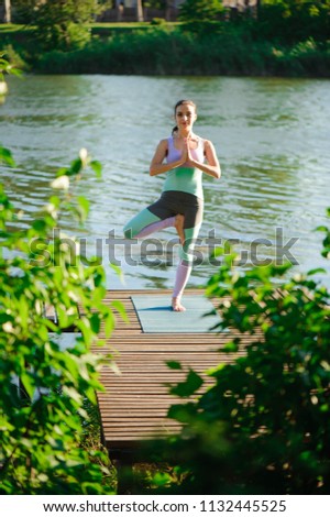 Young woman doing yoga in morning park near lake