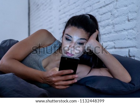 young beautiful Latin woman on bed late at night talking and using mobile phone bored and tired of using smart mobile phone in internet communication overuse concept and smart phone addiction.