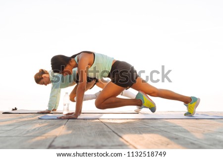 Photo of strong young two sports women friends outdoors on the beach make sport exercises.