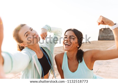 Picture of amazing young sports woman outdoors on the beach make selfie showing biceps.
