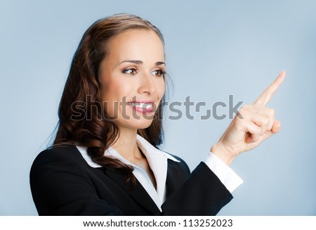 Happy smiling young business woman showing blank area for sign or copyspase, over blue background