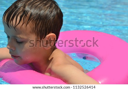 Happy baby boy in a swimming pool with inflatable circle. Cute little baby having fun in the pool. On open air. Sport activities for children.