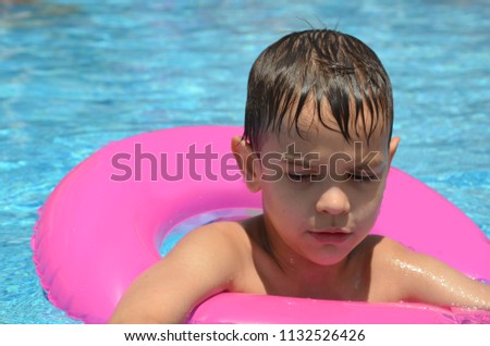 Happy baby boy in a swimming pool with inflatable circle. Cute little baby having fun in the pool. On open air. Sport activities for children.