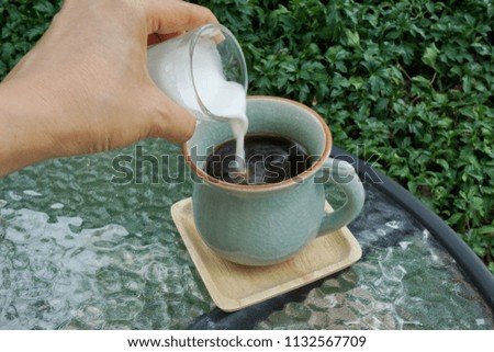 coffee time with sweet smell coffee. cropped image of woman pouring milk  in green cup. milk being poured into a cup of coffee.