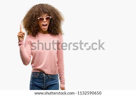 African american woman wearing pink sunglasses pointing finger up with successful idea. Exited and happy. Number one.