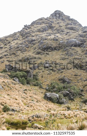 White sky behind rocky peak of a mountain in the Andes. Stone and low vegetation around. Peru. South America. No people.
