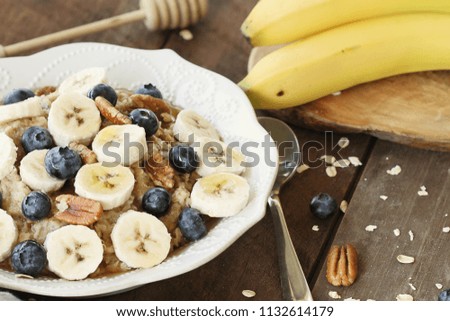 Hot breakfast of healthy oatmeal with pecans, bananas, blueberries and honey over a rustic background. Image shot from overhead.
