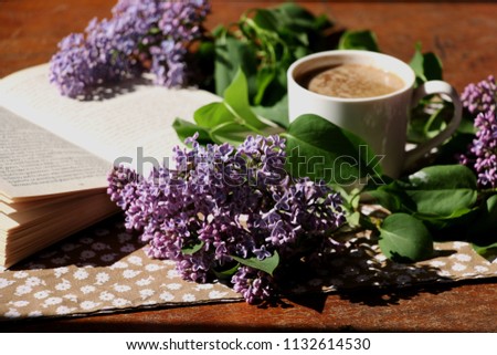Cup of coffee, lilac flowers and an open book on wooden table, romantic background. Royalty-Free Stock Photo #1132614530