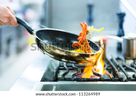 Chef in restaurant kitchen at stove with pan, doing flambe on food Royalty-Free Stock Photo #113264989