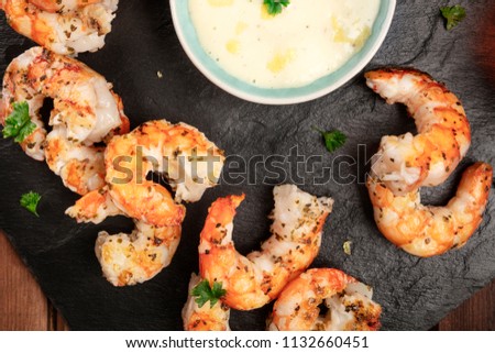 A closeup photo of cooked shrimps on a black plate with a sauce bowl