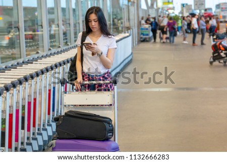 Beautiful Asian woman looks at her smartphone, feeling boring while waiting for her delayed flight. Lovely beautiful woman waiting for her flight. Girl check flight with her smartphone at the airport.
