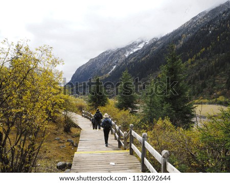 People walking on wooden bridge for sightseeing in autumn season with colorful tress and snow mountain view at Shuangqiao Valley, Siguniang Park