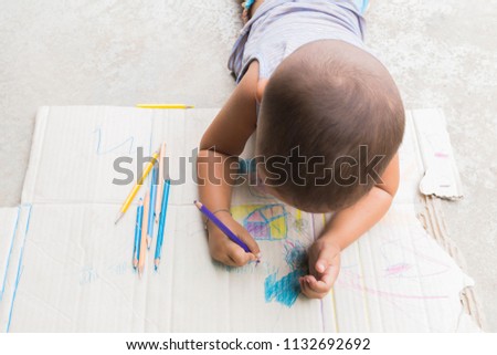 Kid's hands are drawing with colored pencils on sheet of paper.